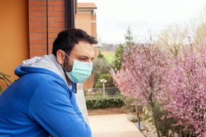 Young caucasian man with mask looking out on the terrace.