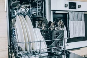 Open dishwasher with white clean dishes after washing in modern scandinavian kitchen.