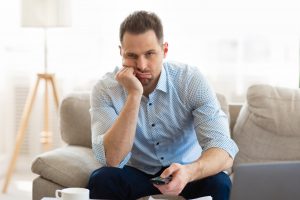 Tired man watching TV at home, holding remote control