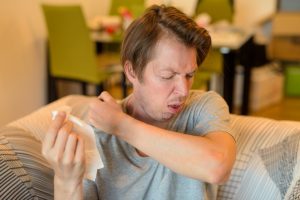 Face of sick young man coughing into elbow while in quarantine at home