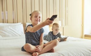Little girl changing channels while watching tv with her brother