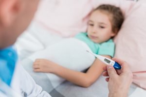 Medical thermometer in hand of pediatrician on background of sick little girl